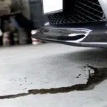 Engine oil leaking under a parked car, forming a small oil puddle on the ground